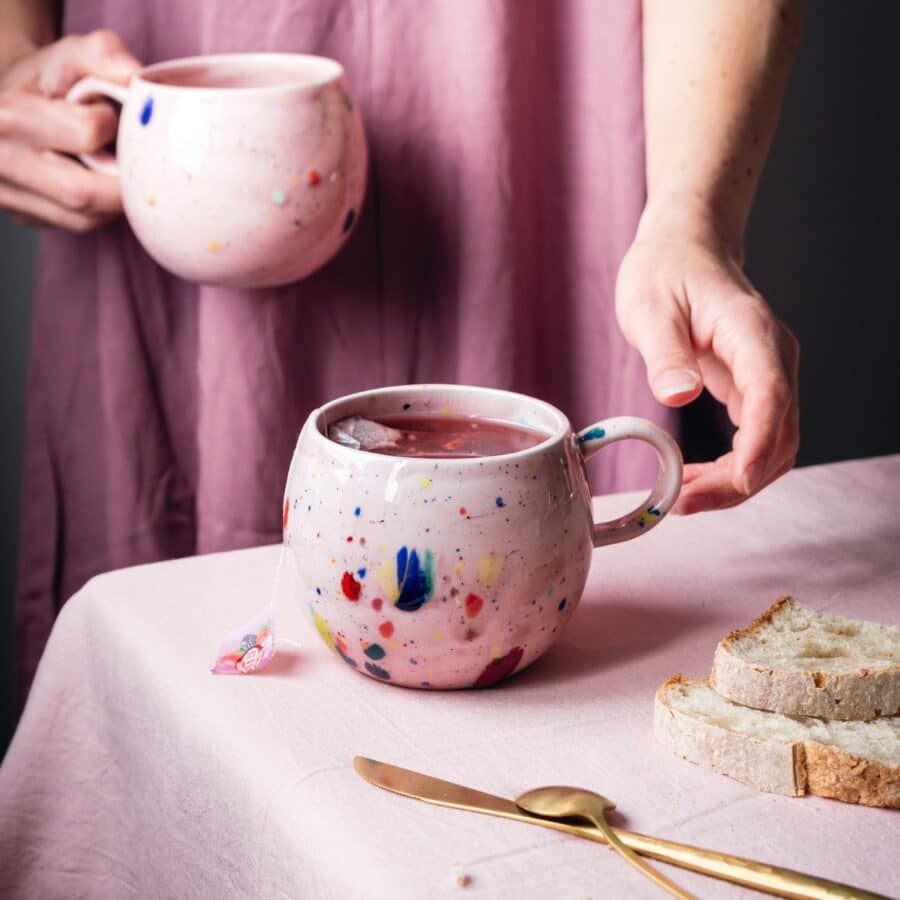 Rosa farbende große Keramik Tasse gefüllt mit Tee in der Hand einer Frau mit Herbst Deko