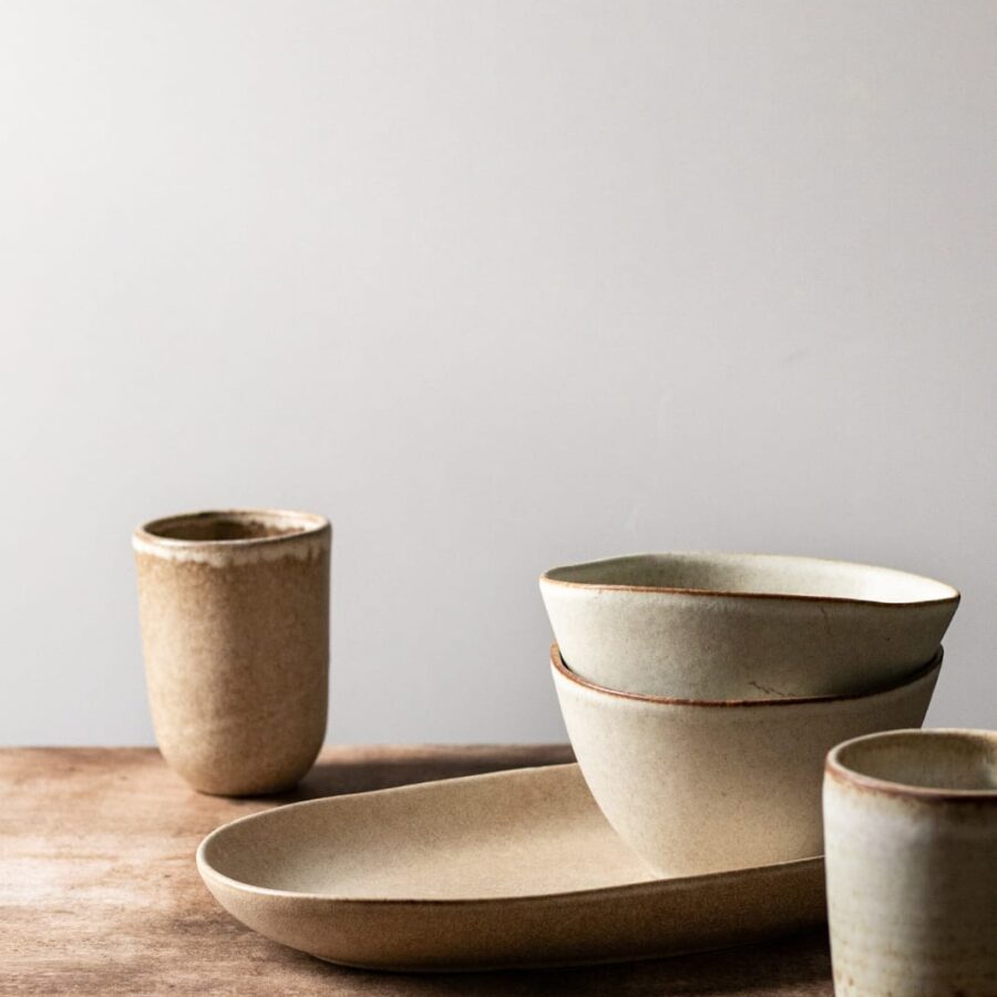 Beige Keramik Schüssel in einander gestapelt auf einem Holztisch mit 2 Keramik Bechern an der Seite